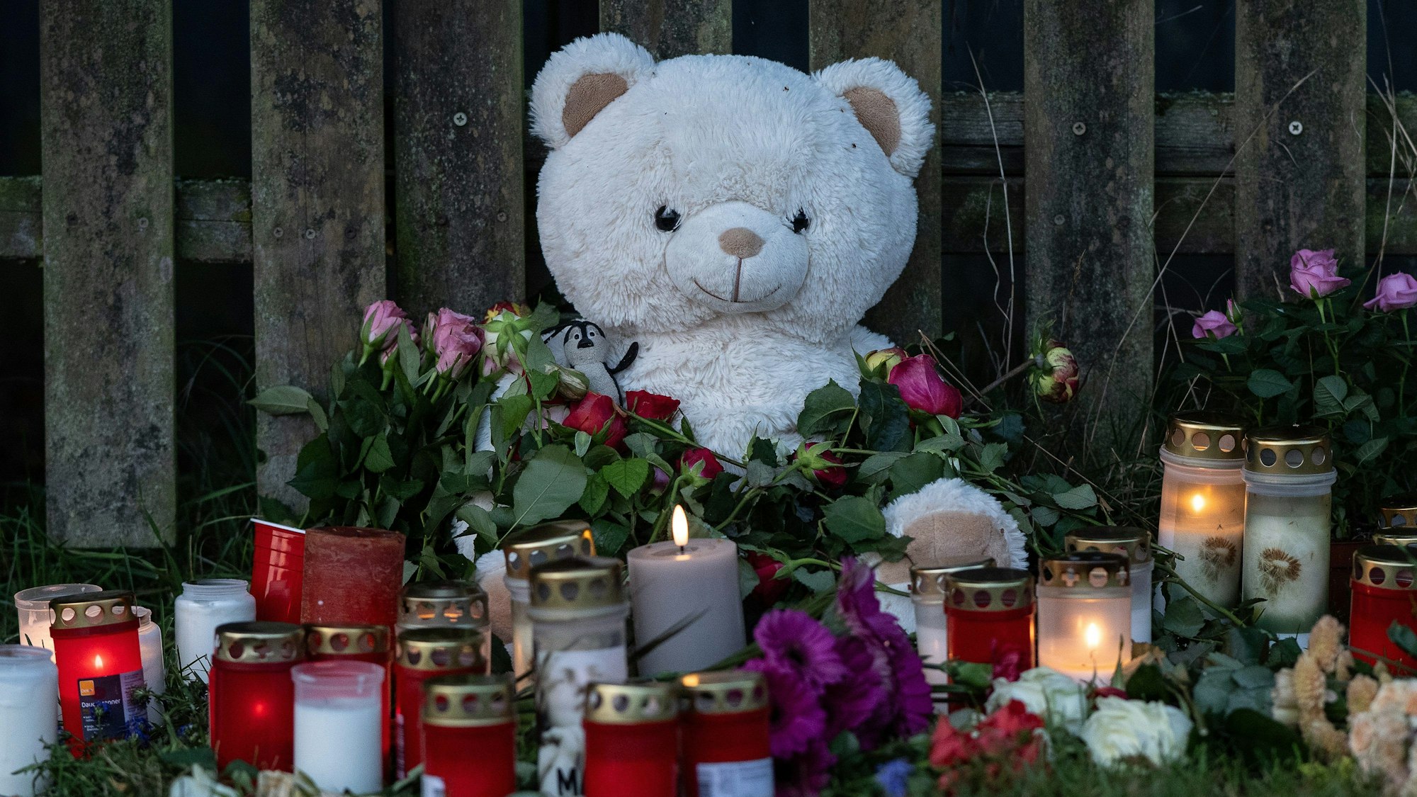 Kerzen, Blumen und ein großer Plüschteddy sind vor einem Zaun am Fundort zu sehen. Am Donnerstag war die Leiche einer vermissten 14-Jährigen aus Nordhessen in einem Waldstück gefunden worden. Die Polizei hat einen Tatverdächtigen festgenommen.