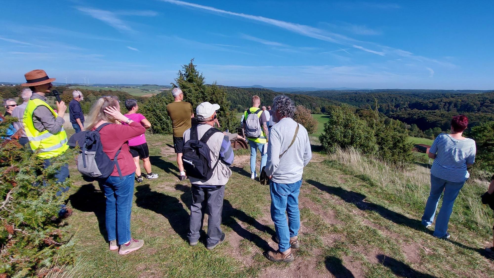 Eine Gruppe Menschen ist von hinten zu sehen. Sie stehen auf dem Kalvarienberg bei Alendorf und genießen bei blauem Himmel die Fernsicht.
