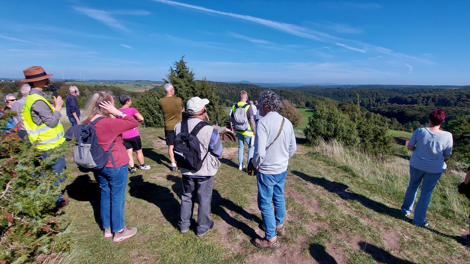 Eine Gruppe Menschen ist von hinten zu sehen. Sie stehen auf dem Kalvarienberg bei Alendorf und genießen bei blauem Himmel die Fernsicht.