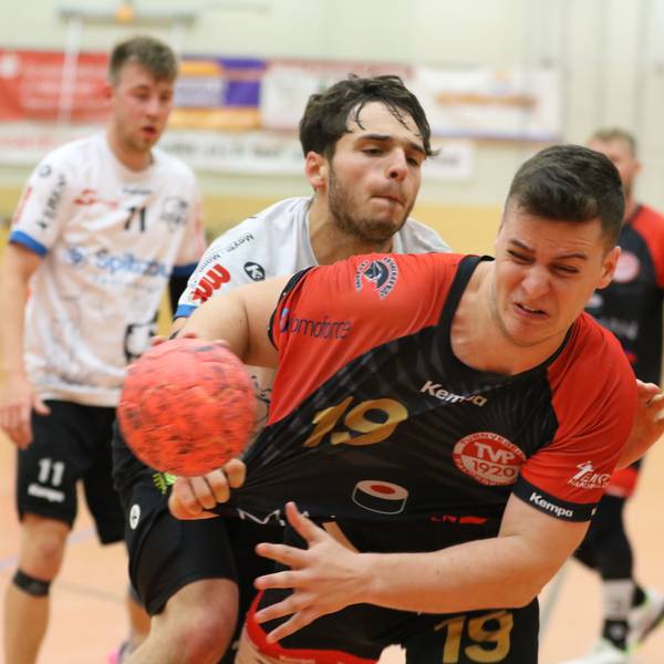 Ein Handballer mit einem Ball in der Hand wird vom Gegenspieler attackiert und am Trikot gezogen.
