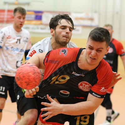Ein Handballer mit einem Ball in der Hand wird vom Gegenspieler attackiert und am Trikot gezogen.
