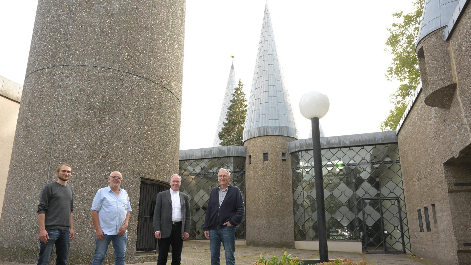 Vor dem Eingang zu Kirche stehen die vier Vertreter der Kirchengemeinde und des Bistums Köln nebeneinander.