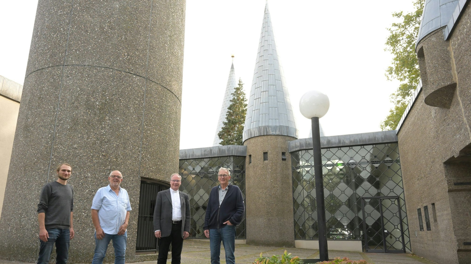 Vor dem Eingang zu Kirche stehen die vier Vertreter der Kirchengemeinde und des Bistums Köln nebeneinander.