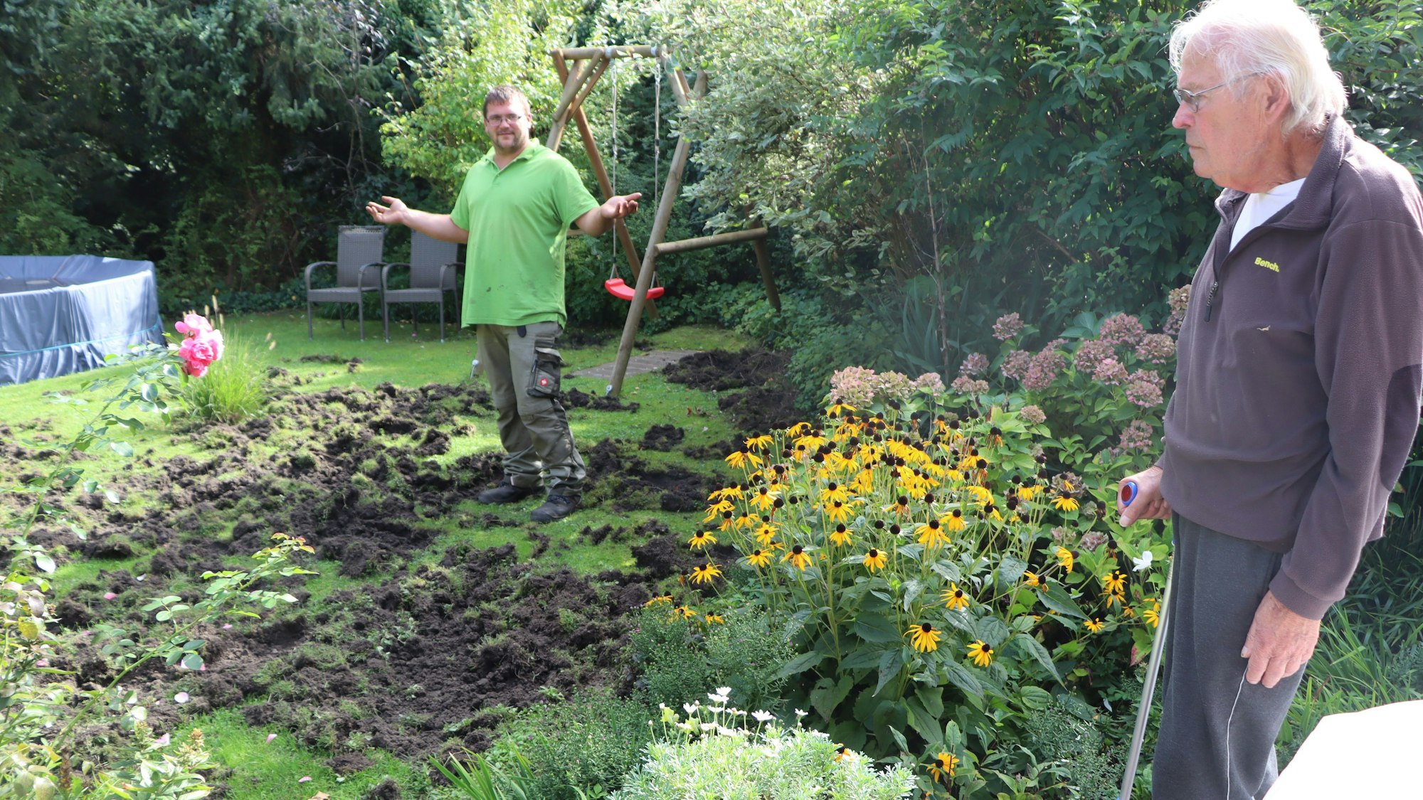 Zwei Männer stehen in einem umgewühlten Garten.