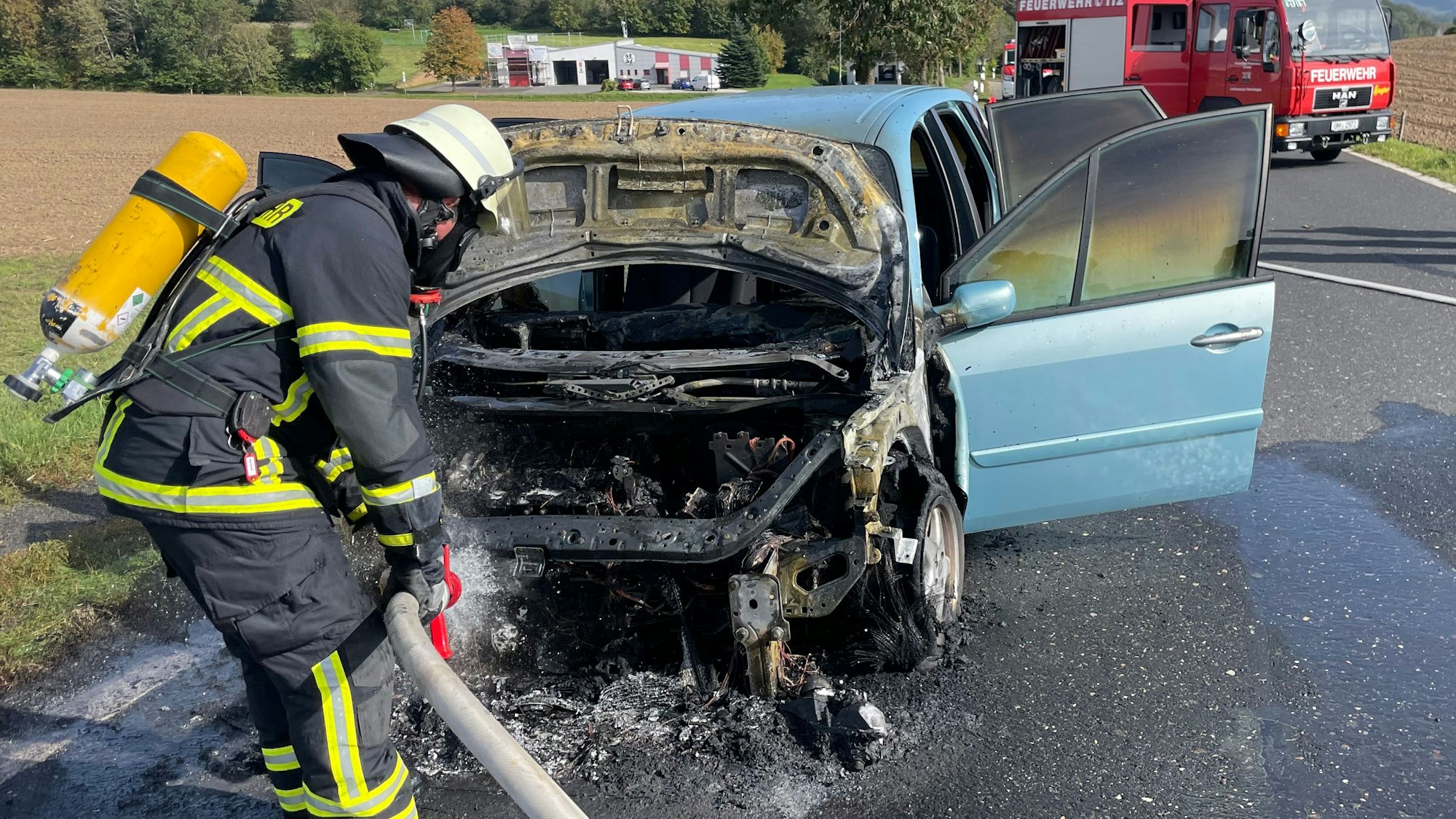Ein Feuerwehrmann löscht ein in der Motorhaube brennenden Pkw.