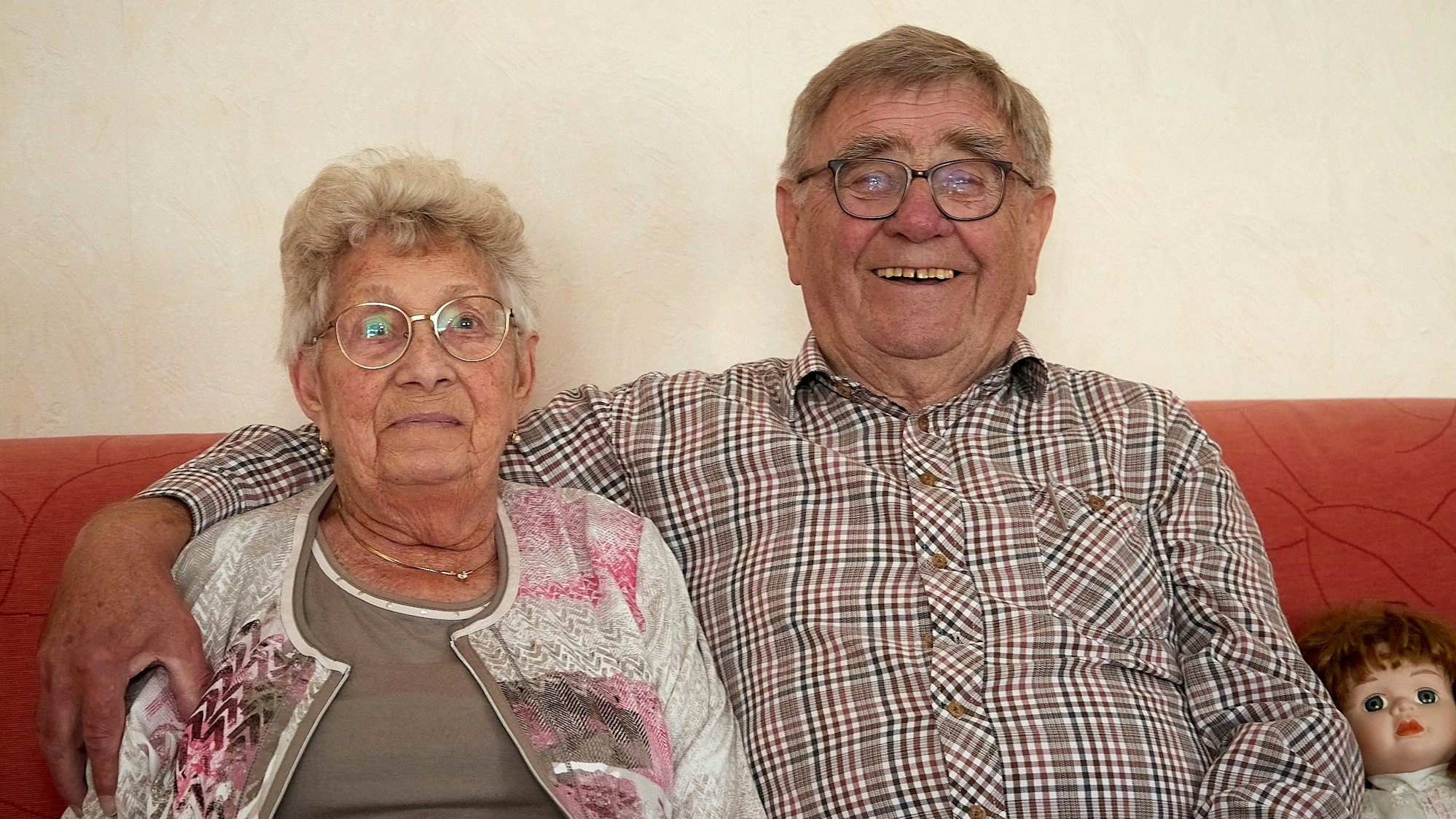 Ein Ehepaar sitzt auf einem roten Sofa: Fritz Bahne legt einen Arm um seine Ehefrau Angelika, mit der er seit 65 Jahren verheiratet ist.