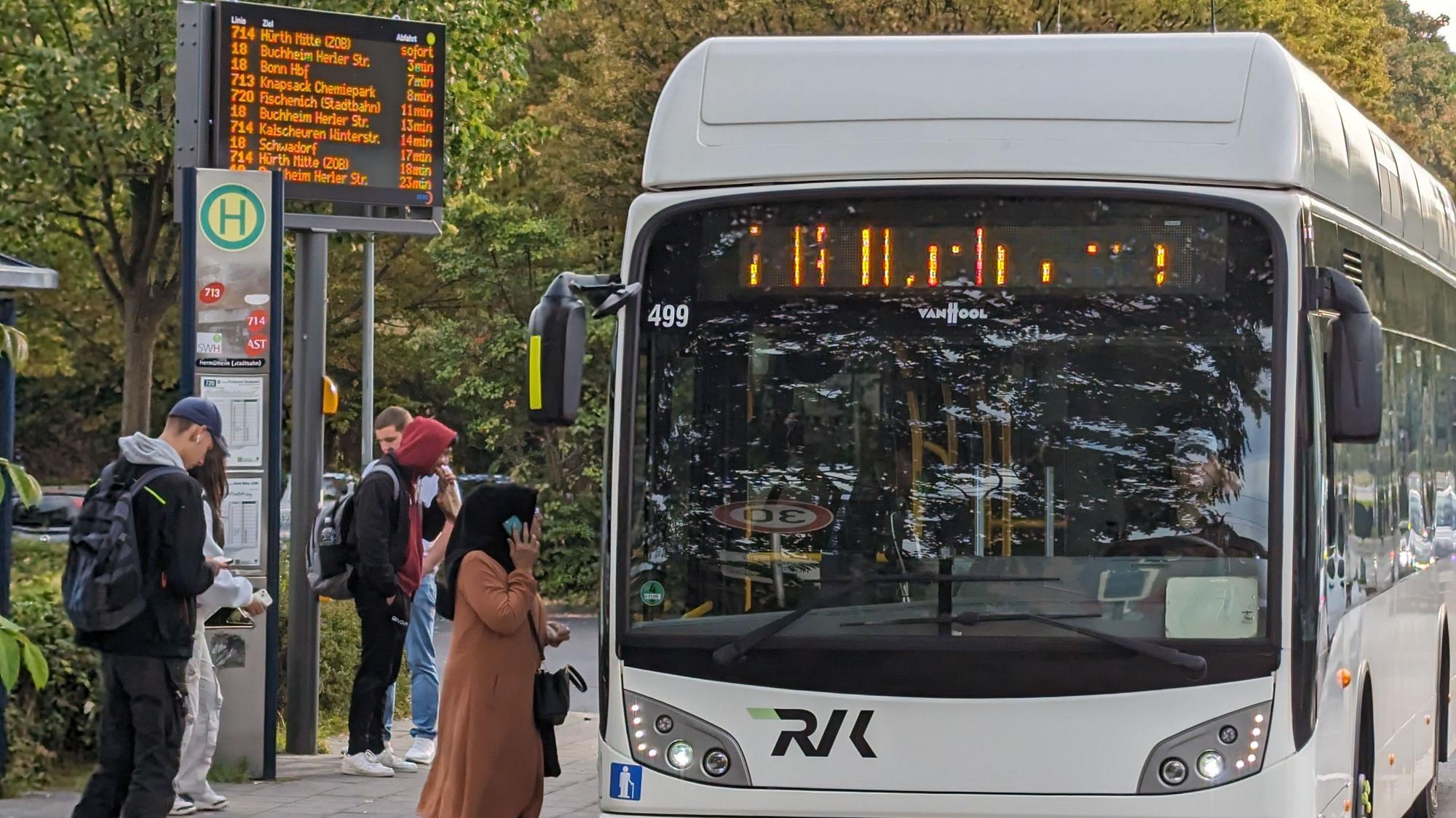 Ein Stadtbus an einer Bushaltestelle mit wartenden Menschen.