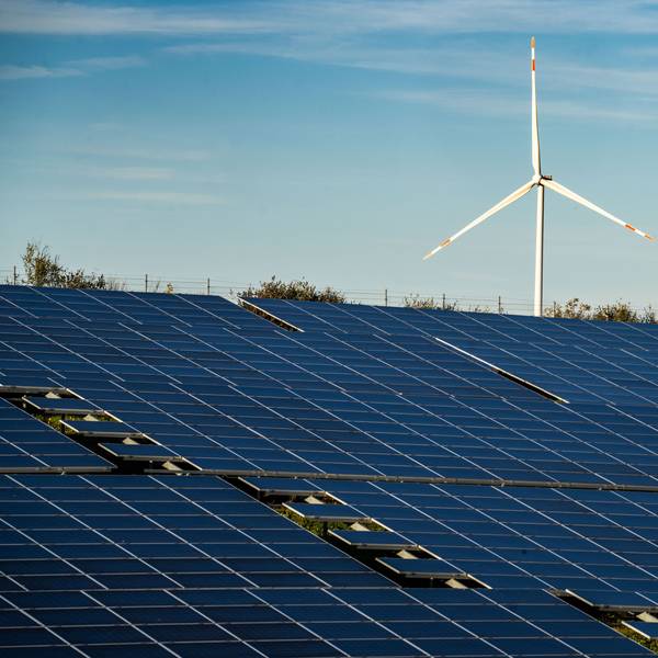 Ein Windrad steht auf einem Hügel oberhalb einer großflächigen Solaranlag.