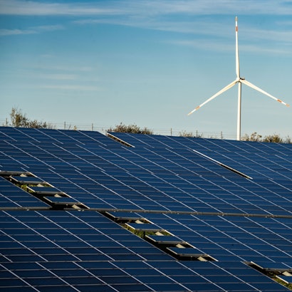Ein Windrad steht auf einem Hügel oberhalb einer großflächigen Solaranlag.