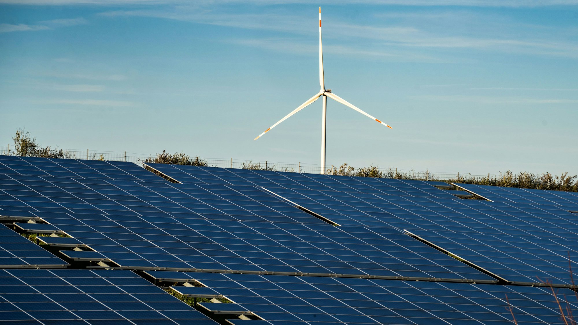 Ein Windrad steht auf einem Hügel oberhalb einer großflächigen Solaranlag.