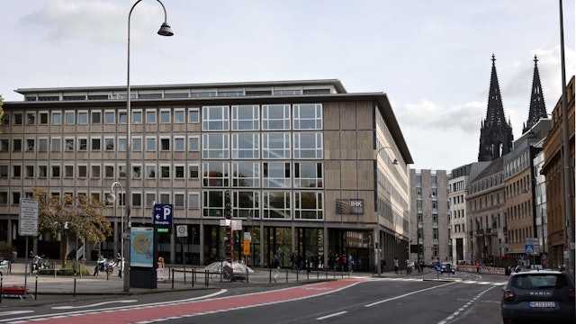 Ein Gebäude mit vielen Fenstern. Im Hintergrund sind die Türme des Kölner Doms sichtbar.