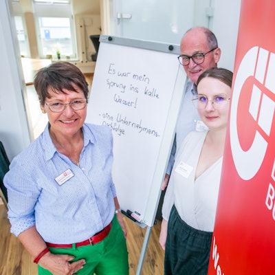 Blick auf drei Menschen vor einer Leinwand.