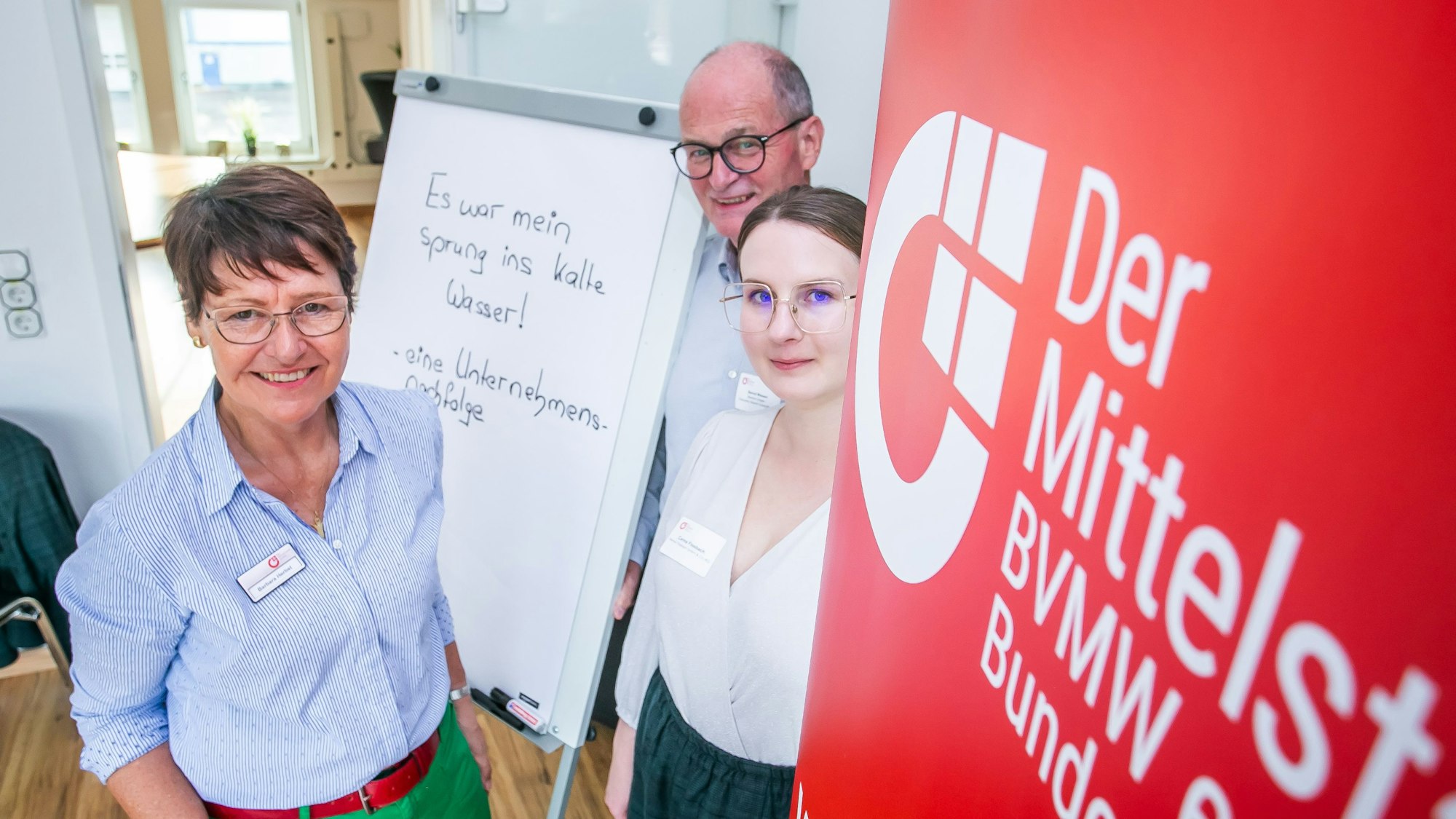 Blick auf drei Menschen vor einer Leinwand.