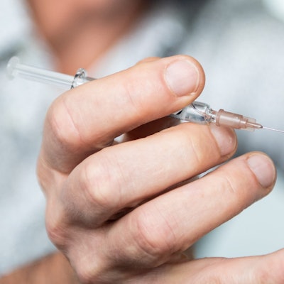 Hand mit einer Spritze an einem nackten Oberarm