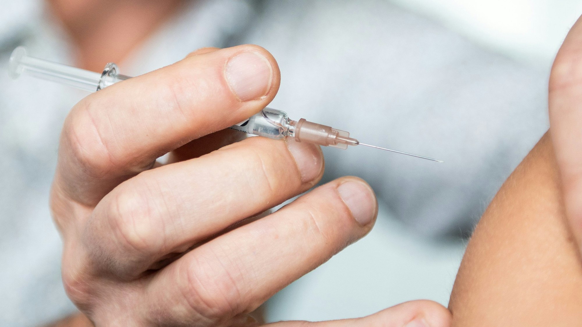 Hand mit einer Spritze an einem nackten Oberarm