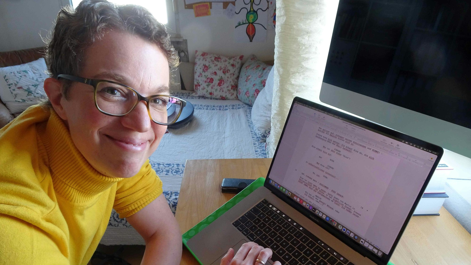 Angela Gilges sitzt vor einem Laptop und lächelt in die Kamera.