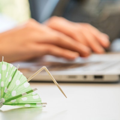 Ein umgeknicktes Papierschirmchen liegt vor einem Laptop auf dem zwei Hande tippen.