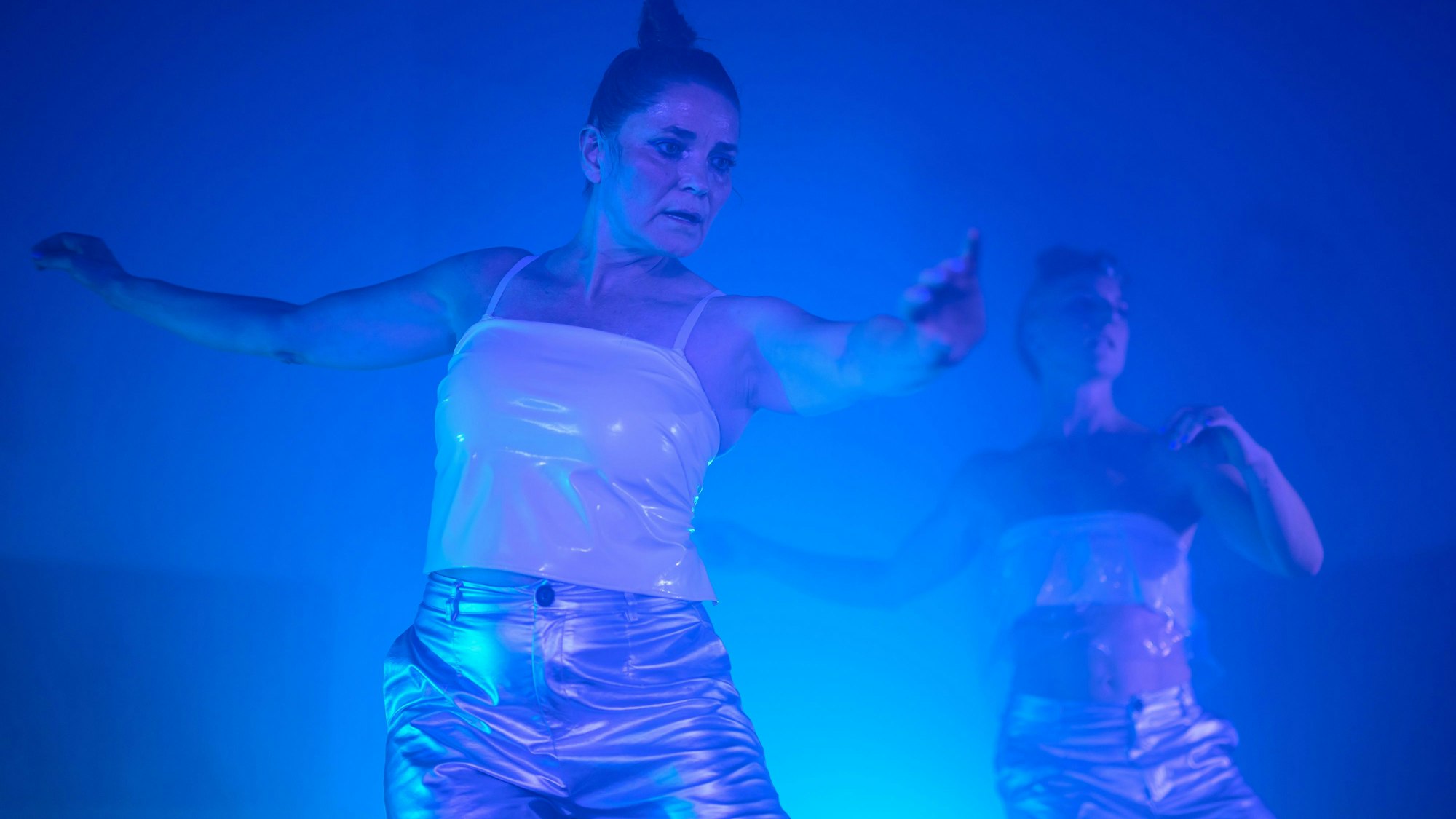 Zwei Tänzerinnen in blauem Licht und in weißen Oberteilen.