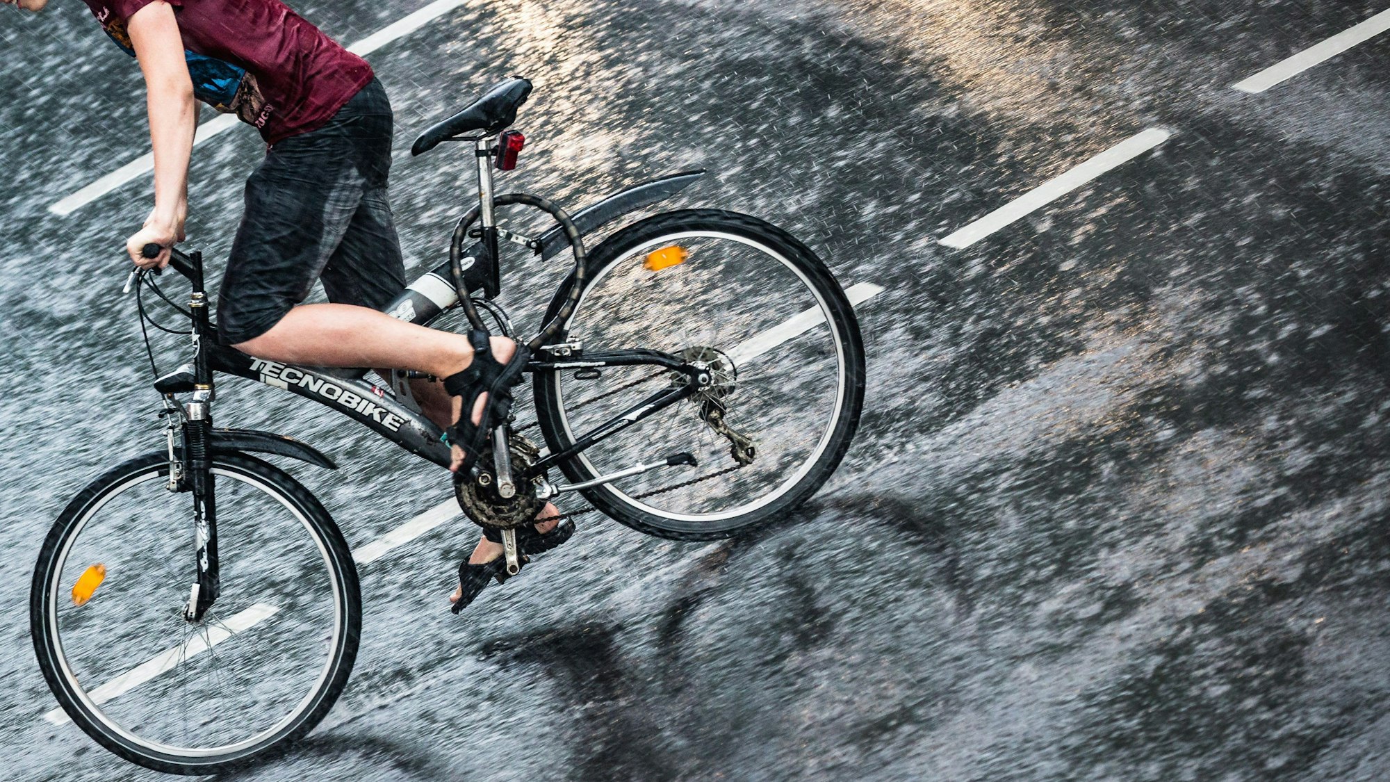 Ein Junge fährt mit seinem Fahrrad während eines Gewitter mit Starkregen über eine Straße.