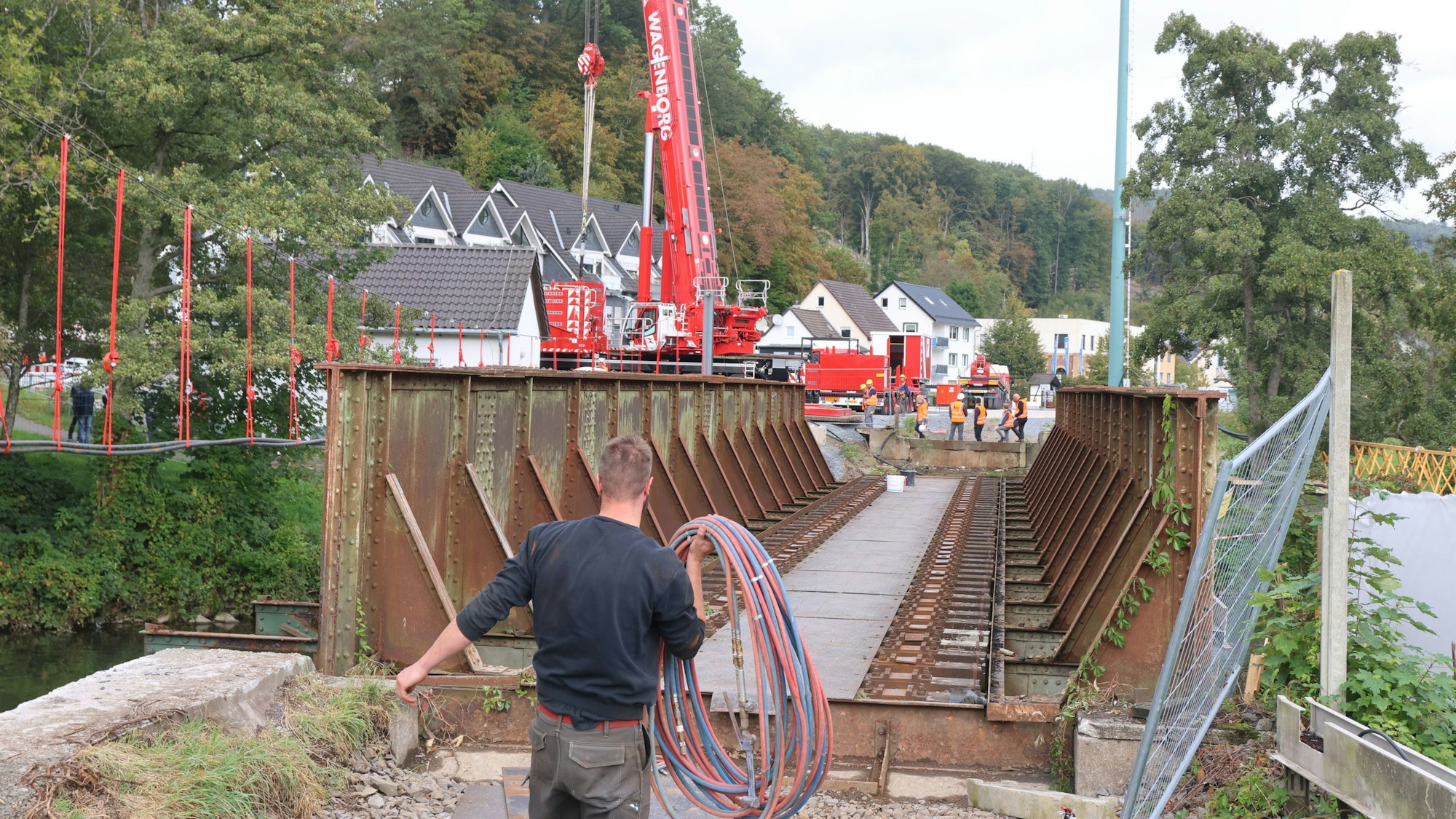 Ein Mann trägt Kabel. Im Hintergrund ist ein Kran an der Aggerbrücke erkennbar.