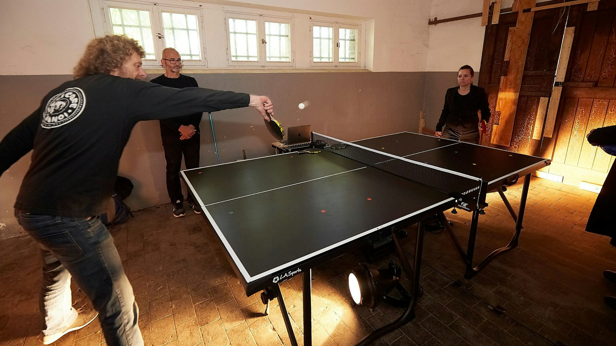 Ein Mann und eine Frau spielen Tischtennis, ein weiterer Mann schaut zu.