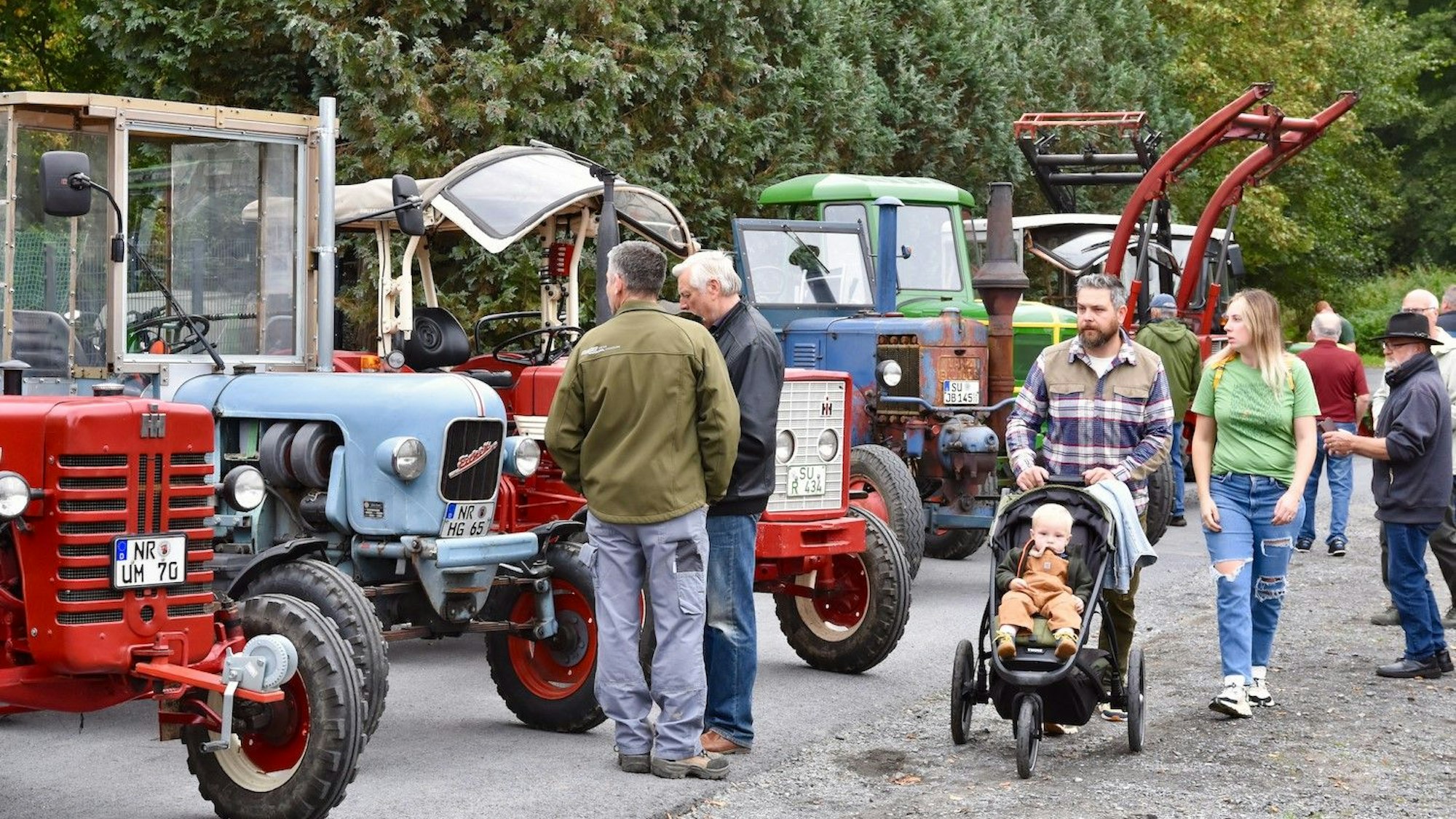 Besucherinnen und Besucher schauen sich die in einer Reihe stehenden alten Trecker an.