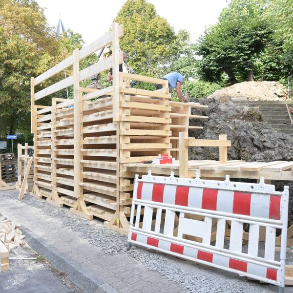 Ein Gerüst aus übereinander montierten Holzbrettern ist vor dem Brunnen montiert.