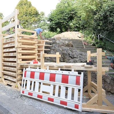 Ein Gerüst aus übereinander montierten Holzbrettern ist vor dem Brunnen montiert.