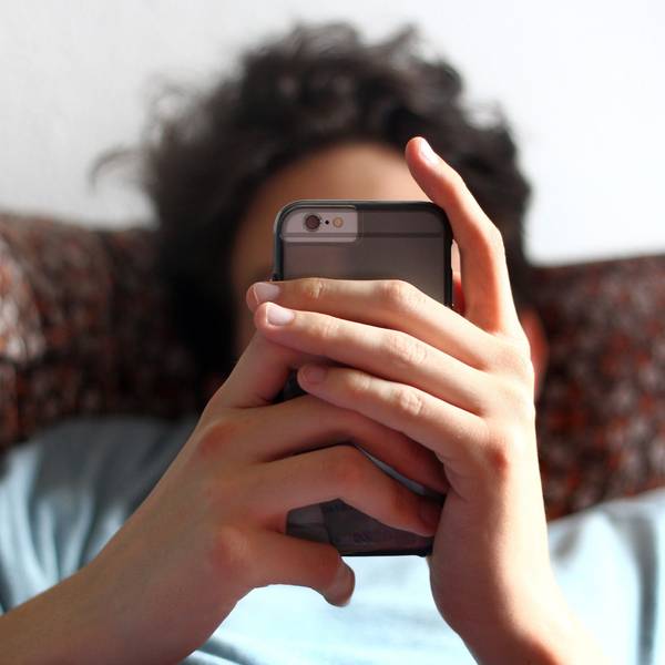 Ein Jugendlicher sitzt auf einem Sofa mit seinem Handy in den Händen.