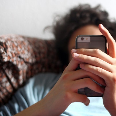 Ein Jugendlicher sitzt auf einem Sofa mit seinem Handy in den Händen.