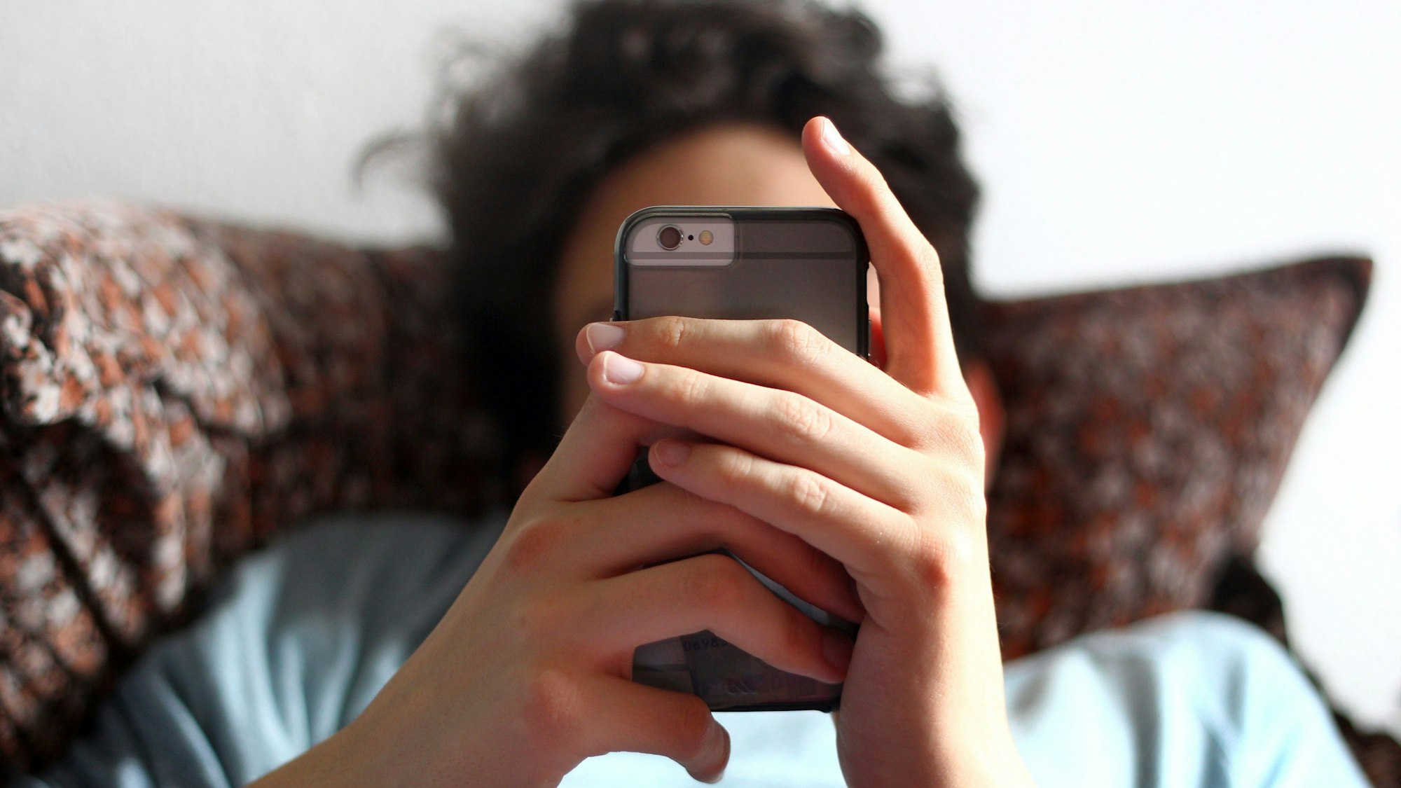 Ein Jugendlicher sitzt auf einem Sofa mit seinem Handy in den Händen.