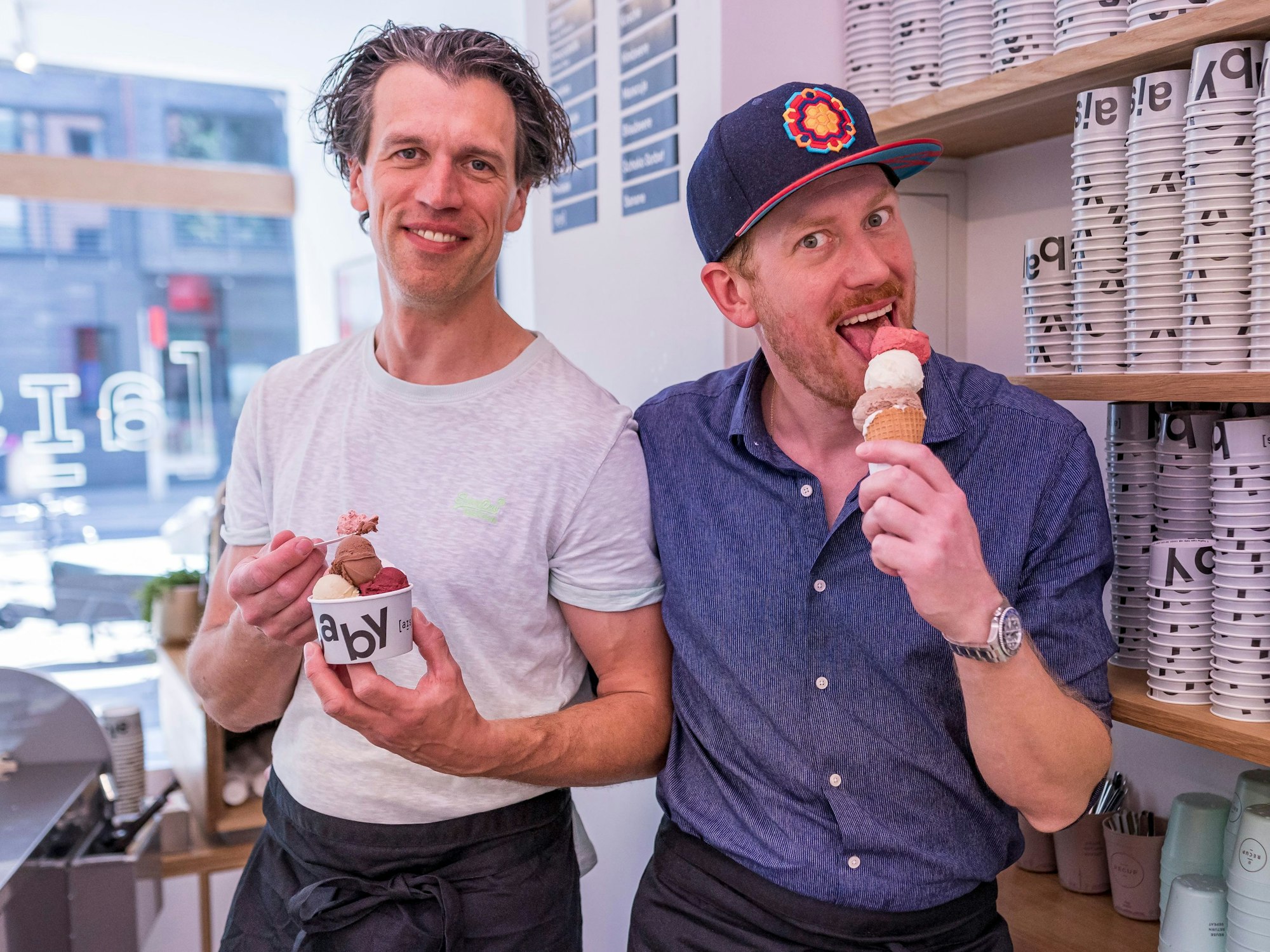 Zwei Männer mit je einem Becher und einem Hörnchen bunter Kugeln Eis in der Hand.