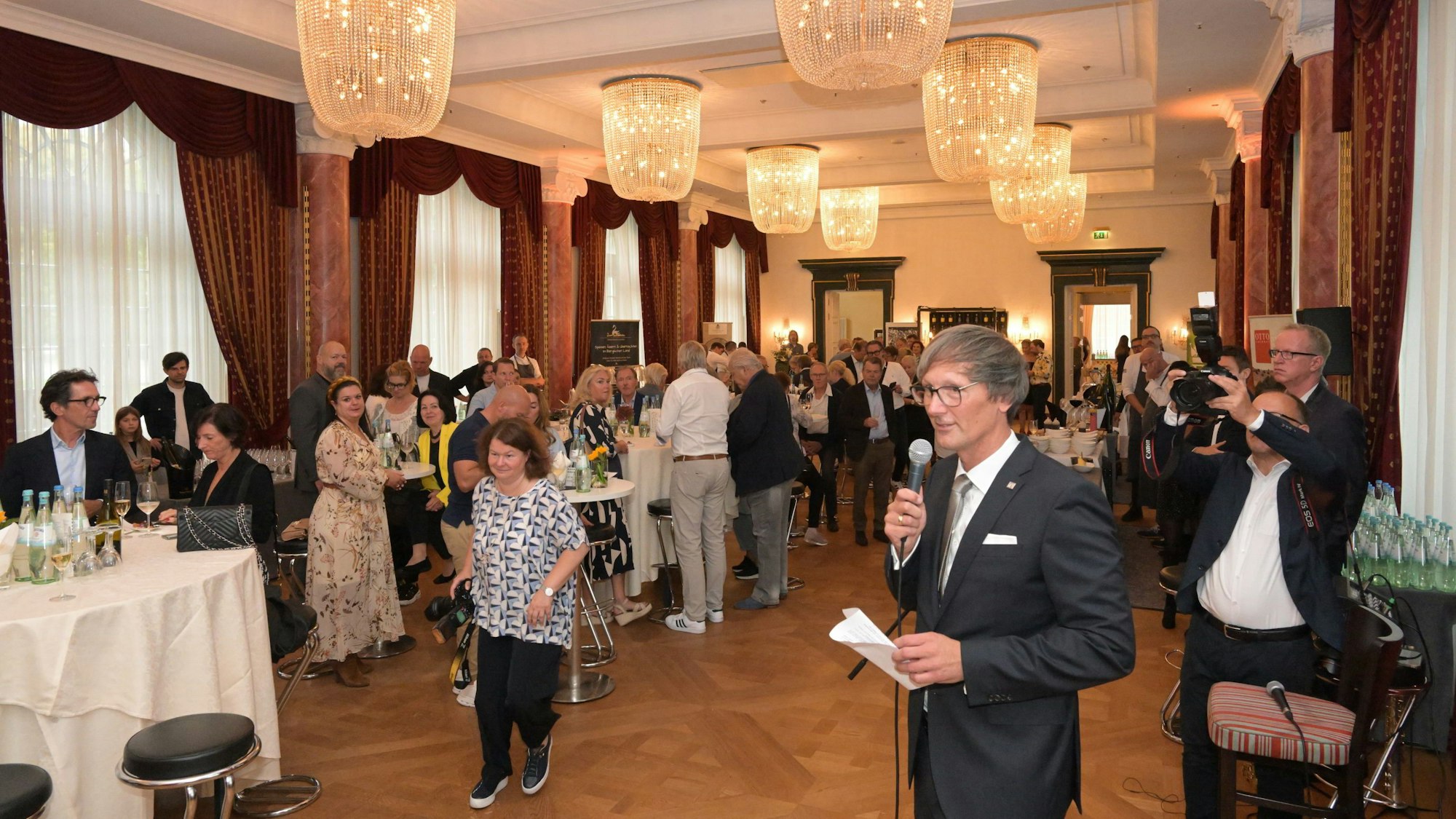 Jörg Stricker steht im Ballsaal vor vielen Menschen und hält ein Mikrofon.