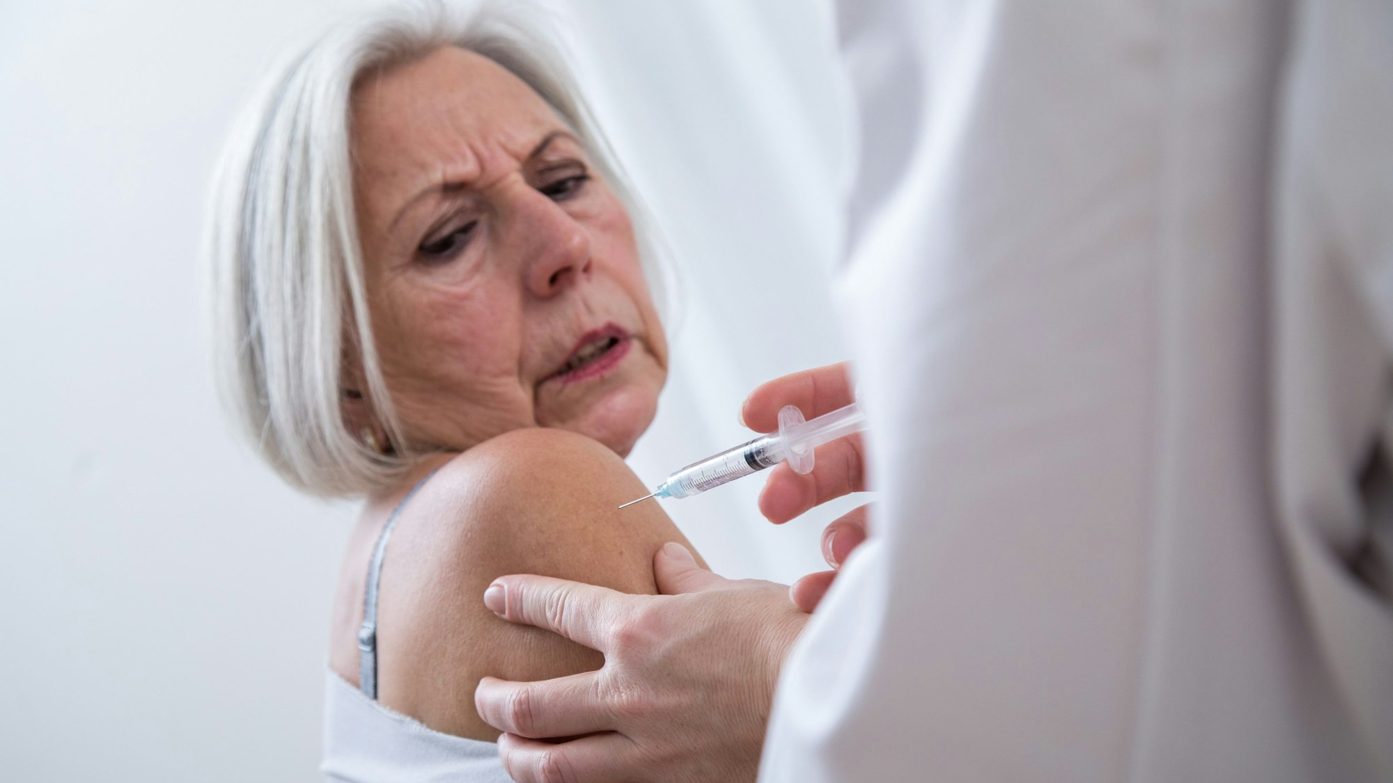 Eine ältere Frau bekommt eine Spritze in den Oberarm.