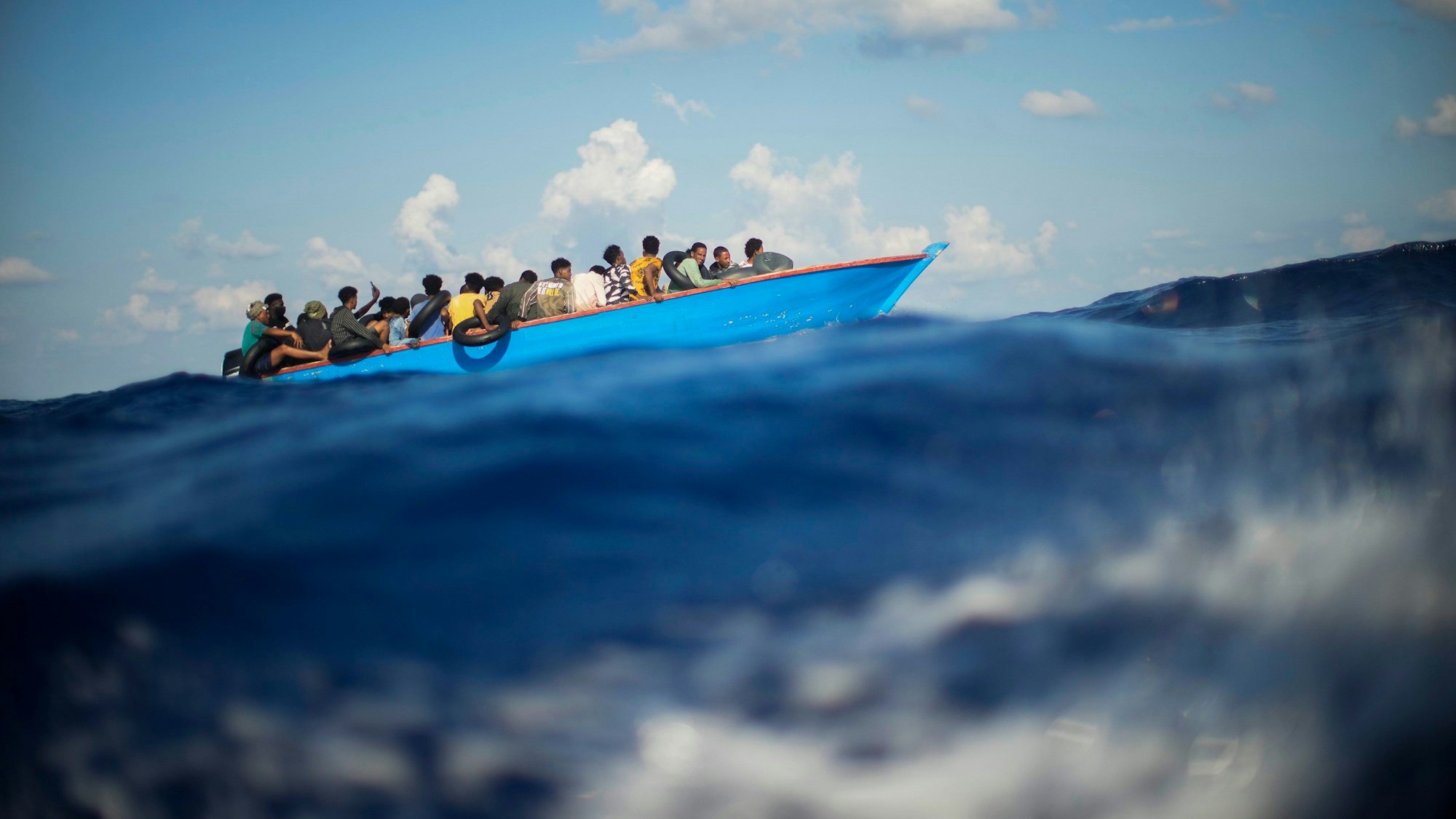 Flüchtende sitzen auf einem Holzboot und fahren über das Mittelmeer, die Aufnahme ist kurz vor der italienischen Insel Lampedusa entstanden. (Archivbild)