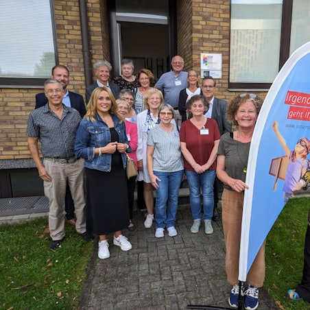 Eine Gruppe von Frauen und Männern vor einem Haus, im Fordergrund zwei Frauen an einer Flagge mit der Aufschrift Lotsenpunkt.