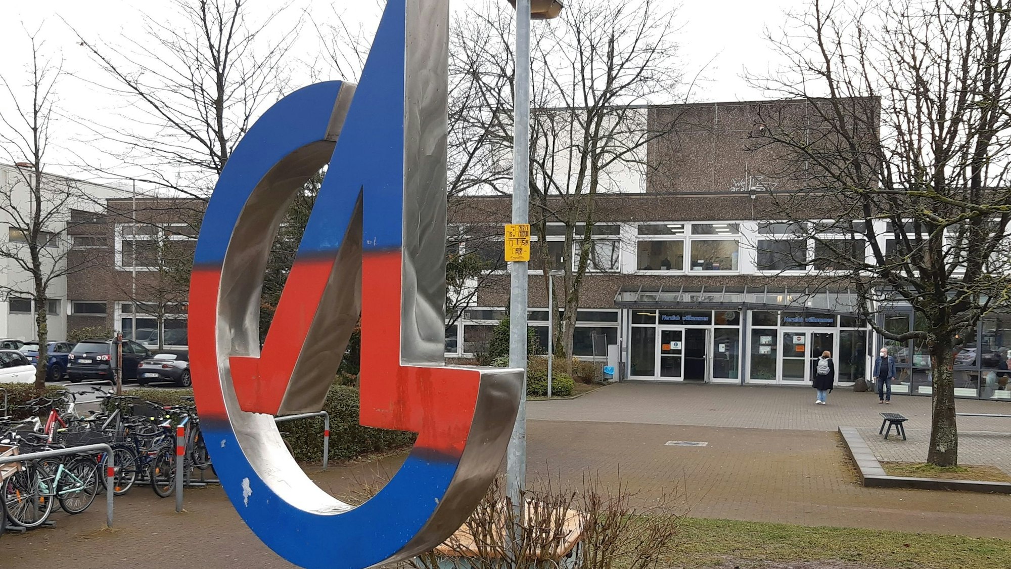 Eine Metallplastik in Blau und Rot zeigt die Buchstaben A und G vor dem Gymnasium in Siegburg
