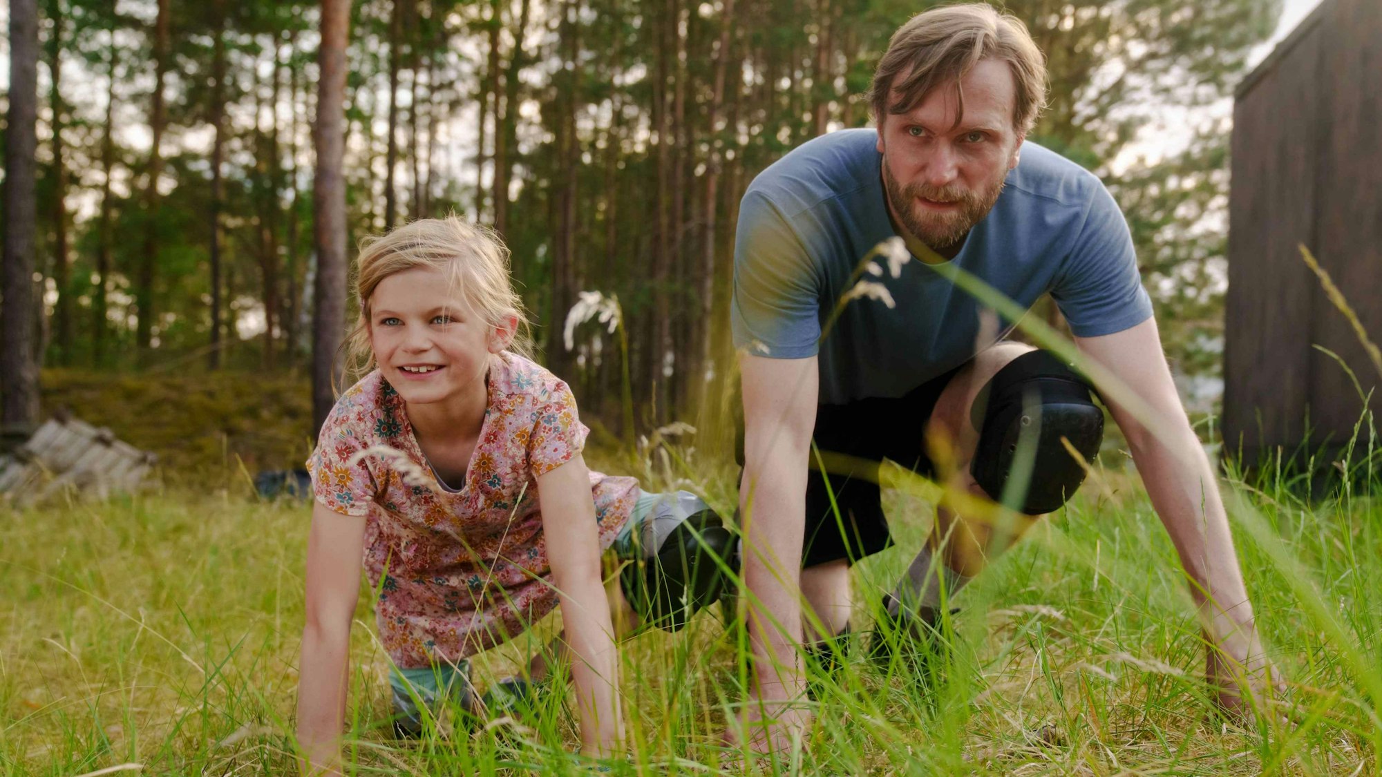 Ein Mann kniet neben einem Mädchen im Gras.