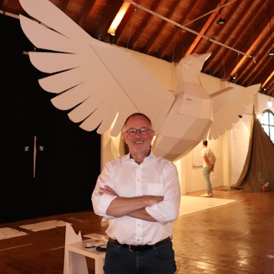 Eine riesige Taube aus Kunststoff hängt in einem Ausstellungsraum, davor steht der Künstler Manni Vogel, der sie gebaut hat.