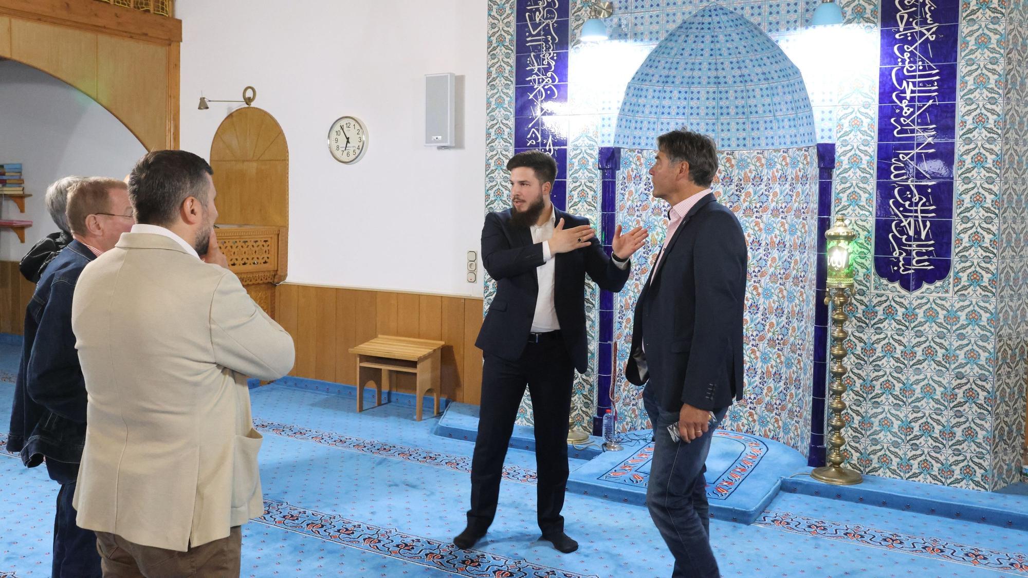 Bei der Moschee-Führung in Bergneustadt erläuterte Mustafa Özgül den Thronvers. Er steht mit Besuchern in einem Gebetsraum der Moschee.