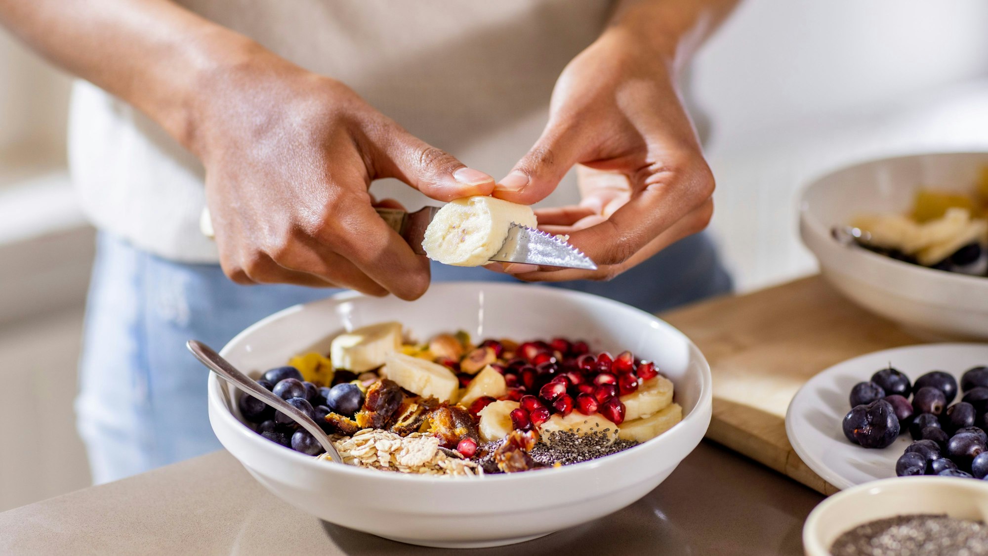 Jemand schneidet Bananenstücke in eine Müsli-Schale.