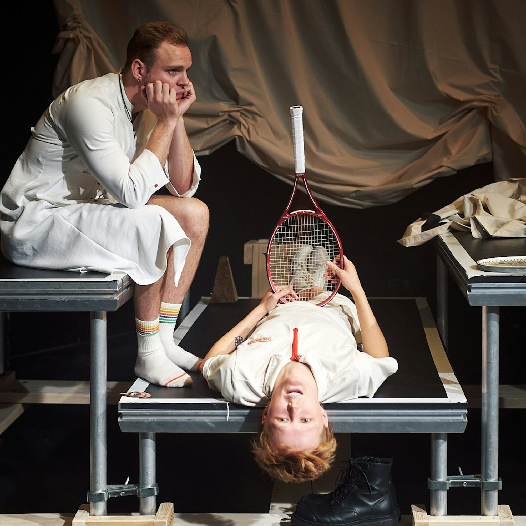 Die Schauspielerin Svea Kirschmeier liegt in ihrer Rolle als „Petra Pan“ auf einem kleinen Podest und hält einen Tennisschläger in der Hand. Ein Schauspielkollege sitzt erhöht neben ihr.