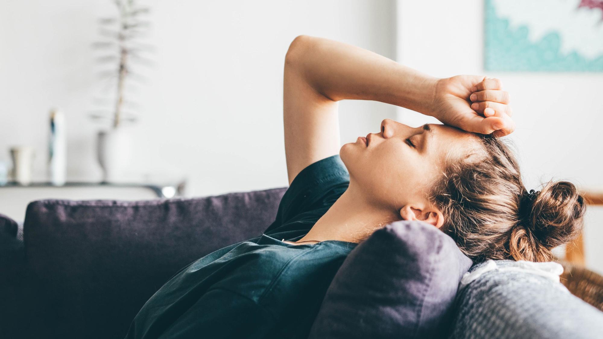 Frau verzweifelt, liegt zu Hause auf dem Sofa. Symbolbild