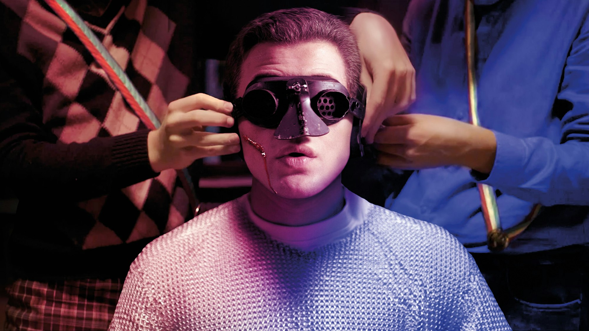 Ein junger Mann im Kettenhemd bekommt eine Maske aufgesetzt.