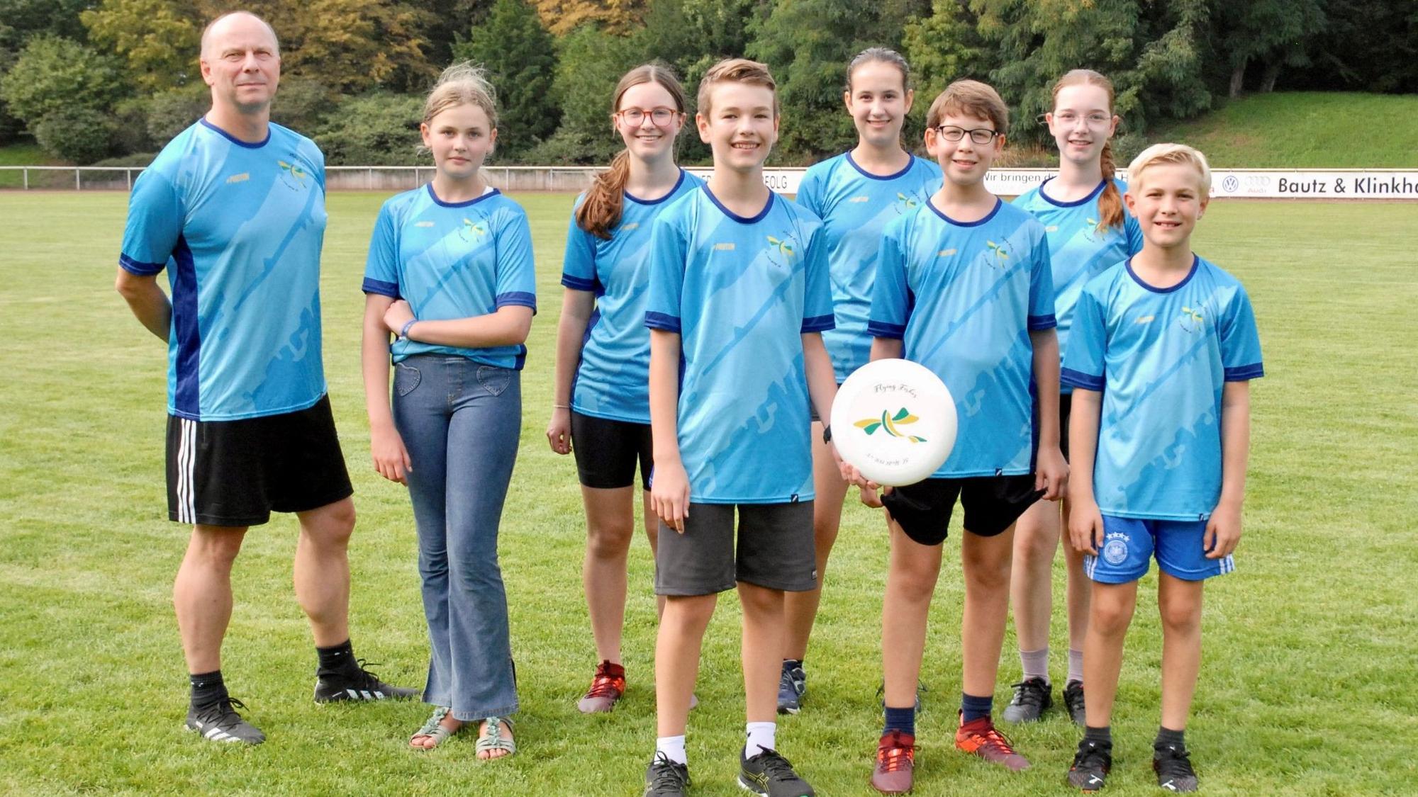 Ein Mann, Mädchen und Jungen stehen in blauen Trikots auf einem Rasenplatz.