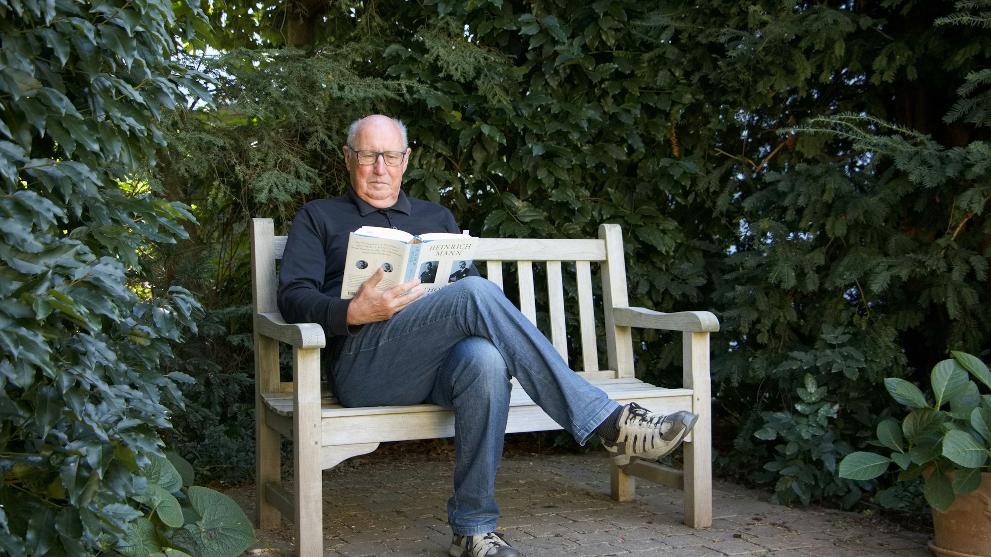 Der Autor Günther Rüther sitzt auf einer Bank im Grünen und liest.