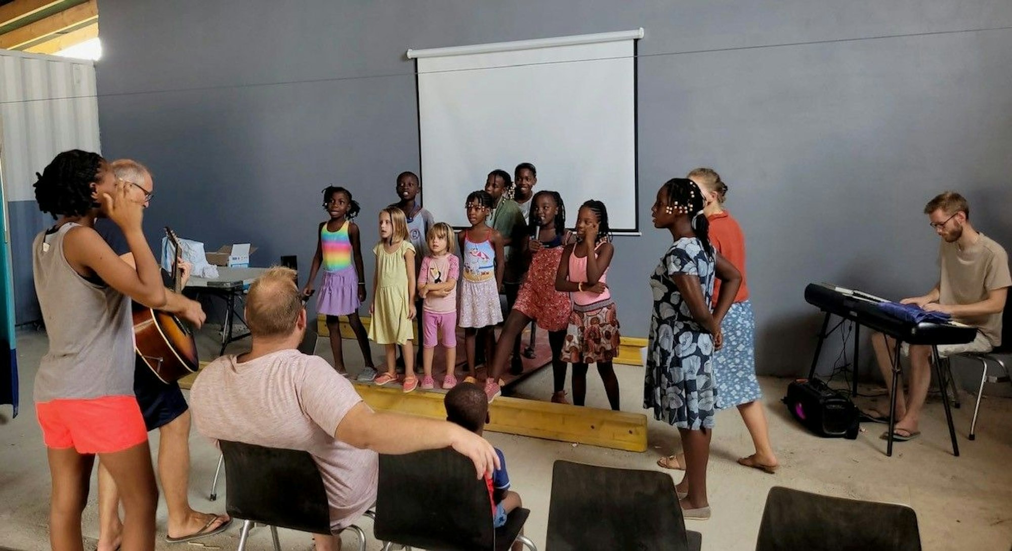 Kinder stehen und singen, zwei Männer begleiten sie an Gitarre und Keyboard