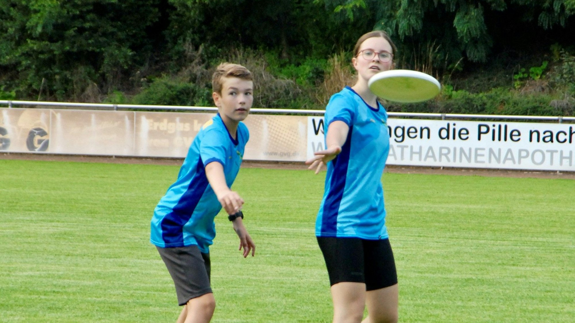 Ein Mädchen wirft eine Frisbee-Scheibe, ein Junge deckt sie.