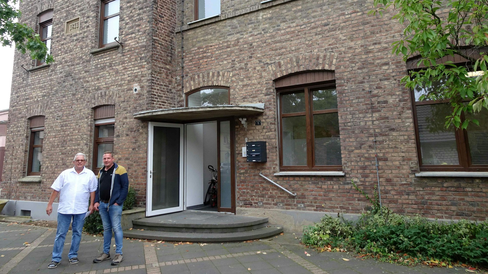 Sitz des Vereins "Lück für os Heematsproch" ist die Alte Schule in Olleim. Im ersten Stock hat der Verein einen großen Raum gemietet, der gleichzeitig Treffpunkt, Besprechungsraum und Büro für die beiden Mitarbeiterinnen ist. Vor der Alten Schule stehen im Gespräch die zwei neuen Mitglieder Heiner Schmacher (links) und der Ollheimer Ortsvorsteher Paul Bison.