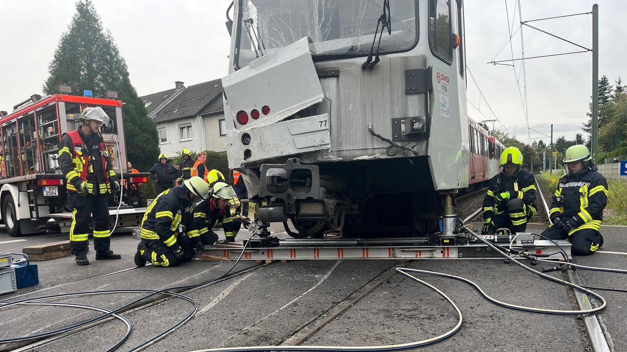 Arbeiter knien rechts und links von der beschädigten Straßenbahn und versuchen, sie mit Arbeitsgeräten anzuheben.
